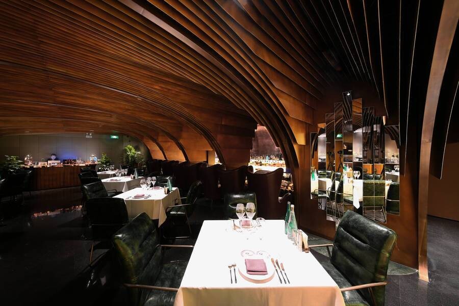 First-floor public dining area with suspended bronze elements and dark flooring forming a theatrical spatial interface.