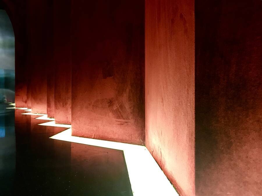 Detail of red velvet curved wall surfaces, with lighting unfolding along the corner and emphasizing the softness of the material.