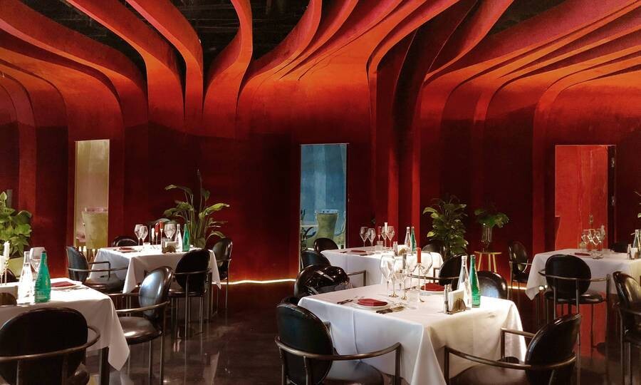 Red-themed private dining room with velvet walls, plants, and a round table forming an intimate dining scene.
