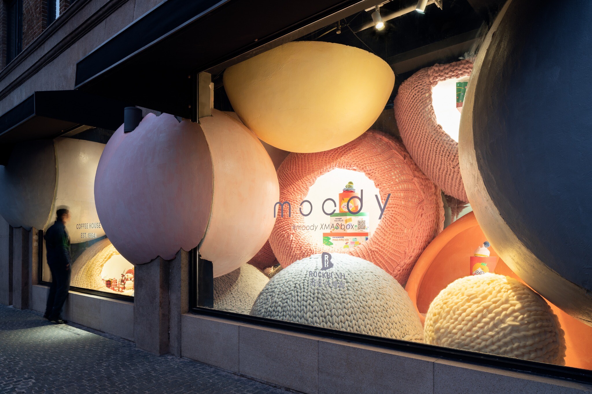 Interior window scene formed by a series of suspended yarn balls, creating an experience between real street view and fictional holiday setting.