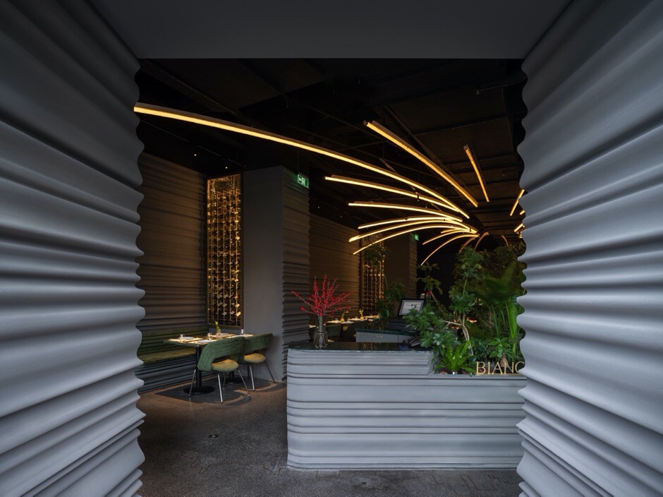 Radiating lighting installation above the main dining area echoing sparks from a grill, working with tables, greenery, and curved space to form the scene.
